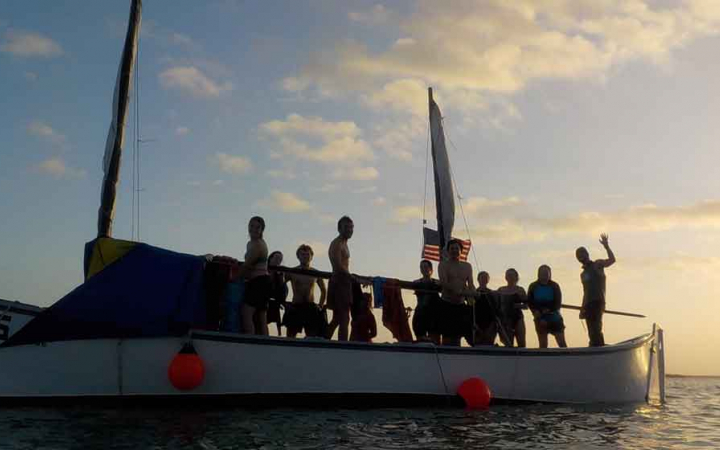 the silhouette of a group of people on a sailboat at sunset